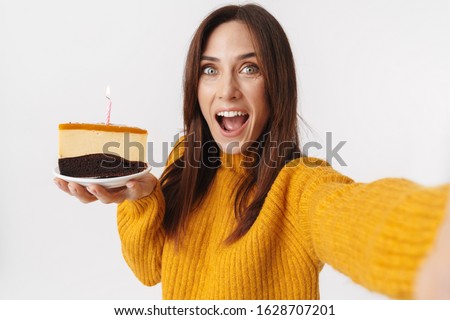 Image of beautiful brunette adult woman wearing sweater holding birthday cake and taking selfie photo isolated over white background