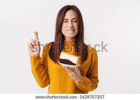 Image of beautiful brunette adult woman wearing sweater holding birthday cake and making wish isolated over white background