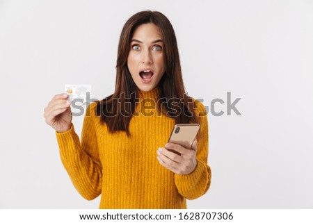 Image of excited brunette adult woman wearing sweater holding cellphone and credit card isolated over white background