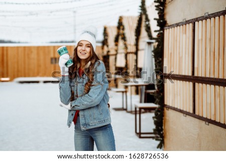 A young beautiful girl in a winter hat poses against the background of the year decorated for Christmas. Woman holding a Cup of coffee