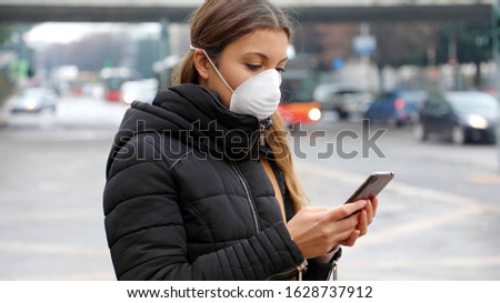 COVID-19 Pandemic Coronavirus Mobile Application - Young Woman Wearing Face Mask Using Smart Phone App in City Street to Aid Contact Tracing in Response to the 2019-20 Coronavirus Pandemic Royalty-Free Stock Photo #1628737912