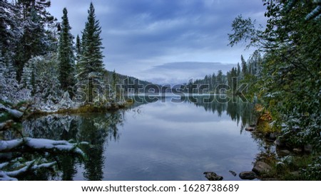 A calm water lake with visible snow remnants on the trees surrounding it, Alberta, Canada.