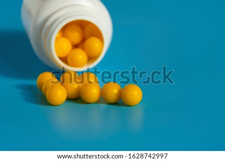 Yellow vitamins pour out from a pill bubble on a blue background. Vitamin complex. Multivitamins to enhance health and immunity. Medical concept
