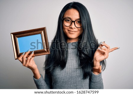 Young beautiful chinese woman holding vintage frame over isolated white background very happy pointing with hand and finger to the side