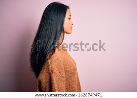 Young beautiful chinese woman wearing casual sweater over isolated pink background looking to side, relax profile pose with natural face with confident smile.