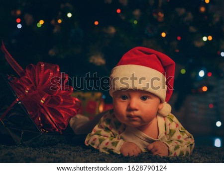 A small child in a Santa Claus hat on the background of a Christmas tree with gifts. New year and Christmas.