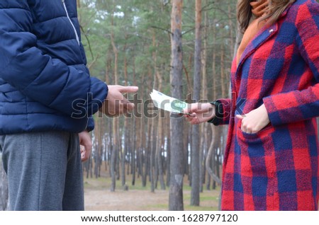 Girl transfers euro bills to the hands of a young guy in forest. Concept of robbery or illegal deal transaction