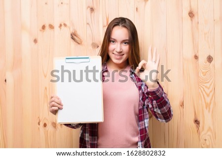 young blonde pretty girl with a paper sheet against wood wall