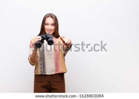 young blonde pretty girl holding a binoculars against white wall
