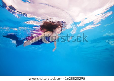 girl in a mermaid costume poses underwater in a pool.