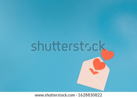 A few red hearts pop out from a light pink envelope on a blue background