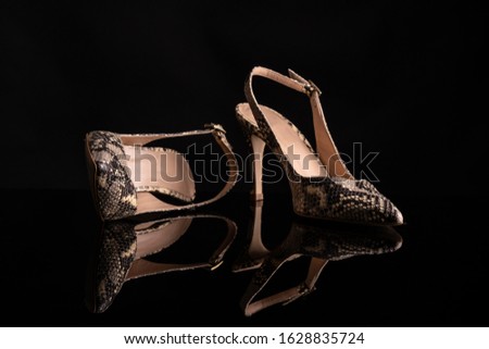 woman snake skin shoes print on black background supported on black surface reflecting shoes