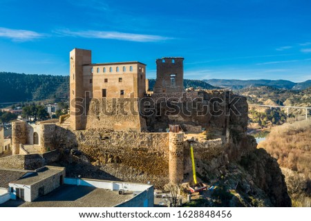 Aerial panoramic view of medieval partially restored Cofrentes castle above the Cabriel river in Spain with reflection and dramatic sky