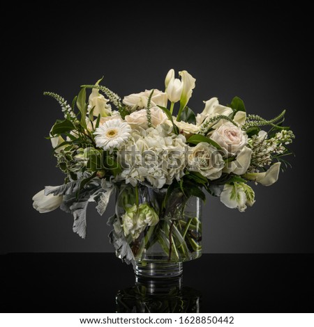 Studio photography of floral arrangements on a gray backdrop with white and pink roses, geraniums and other wild flowers