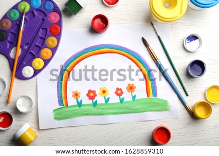 Flat lay composition with child's painting of flowers and rainbow on white wooden table