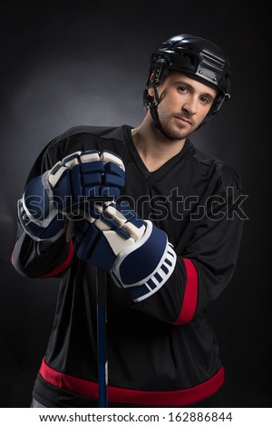 Attractive young hockey player posing on camera. Standing isolated on black 