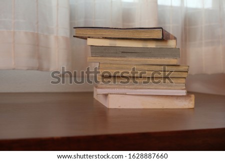 Close up of stack or pile of old book that place on a table near to the window and curtain with blurred background 