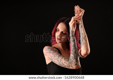 Beautiful woman with tattoos on arms against black background. Space for text