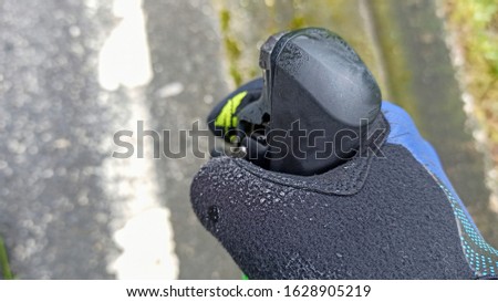 Cyclist hand in a black glove with yellow and blue decoration, full of water drops on the thumb and grab the right lever of the road bike changes, in the background with the road and blurred vegetatio