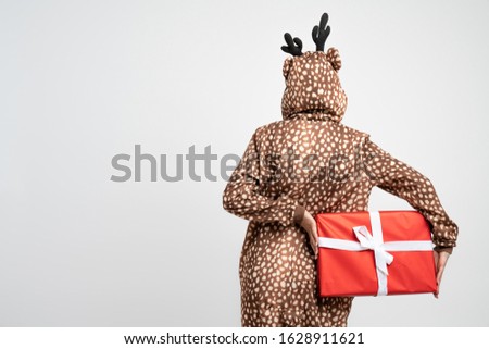Female in giraffe pajama standing bag to the camera and holds big red gift box in hads, isolated over white background, studio photo