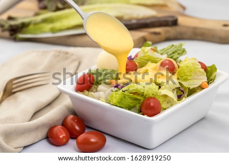A studio image of a salad topped with cherry tomatoes and dressing being poured on it. Royalty-Free Stock Photo #1628919250