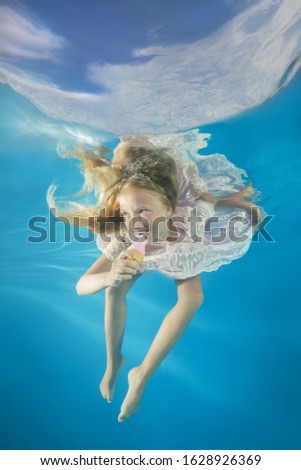 Girl in white dress eating ice cream underwater. Young beautiful girl poses underwater in the pool.  
