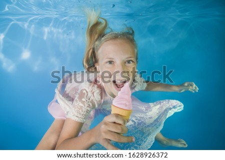 Girl in white dress eating ice cream underwater. Young beautiful girl poses underwater in the pool.  