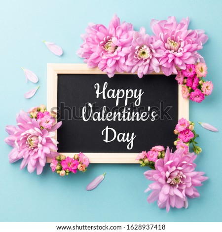 Happy Valentine Day. Pink flowers and chalkboard frame on blue background. Top view. Space for text. 