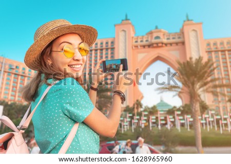 Happy asian girl traveller taking pictures of the famous luxury Atlantis hotel building on a Jumeirah Palm Island in Duba, UAE.