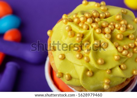 Birthday cupcake in funny polka dot colorful cups stack and deflated balloons on violet background, close up, copy space
