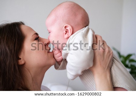 Mother love. Close up caucasian young brunette woman looking to her little cutest infant baby. Mom kissing her son at home. Happy motherhood.