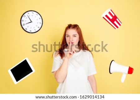 Whispering secrets. Caucasian young woman's portrait on yellow studio background, too much tasks. How to manage time right. Concept of working, business, finance, freelance, self management, planning.