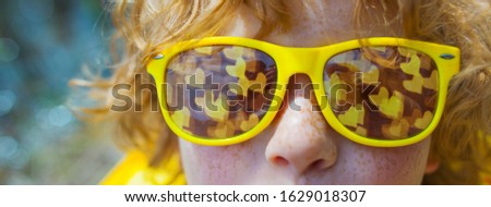 Happy kid in yellow sunglasses. Close up portrait of caucasian boy with freckles in yellow sunglasses, mirror reflection in glasses is  bokeh with hearts, yellow clothes, red hair.