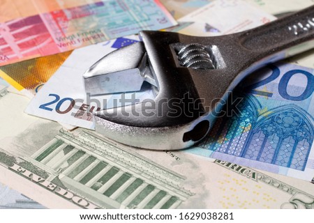 Adjustable wrench on a stack of various Euro, US dollar and Swiss franc banknotes.