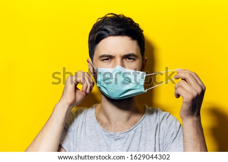 Portrait of young man, takes off the medical flu mask, on background of yellow color. Royalty-Free Stock Photo #1629044302