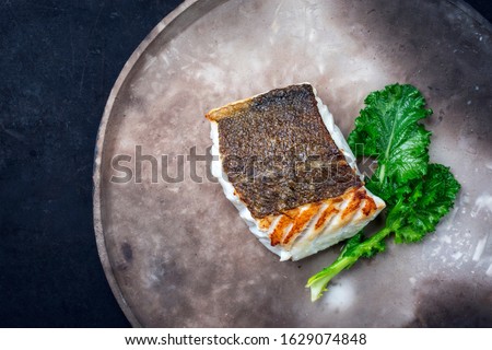 Gourmet fried European skrei cod fish filet with rapini broccoli rabe as top view on a modern design plate with copy space left 