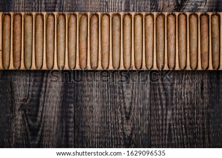 Cigars in wooden box on old table. Cigar manufacturing in vintage traditional scale tools, top view. Old box with handmade cigars in wooden humidor.  Royalty-Free Stock Photo #1629096535