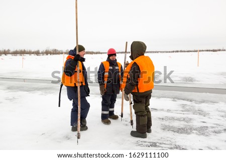 Installers with hooks in their hands are talking on the ice of the lake