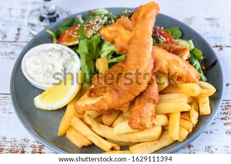 A plate of 'Fish and Chips' with battered fish, potato chips, salad, tartar sauce and lemon wedge. Royalty-Free Stock Photo #1629111394