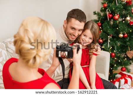 family, christmas, x-mas, winter, happiness and people concept - mother taking picture of smiling father and daughter