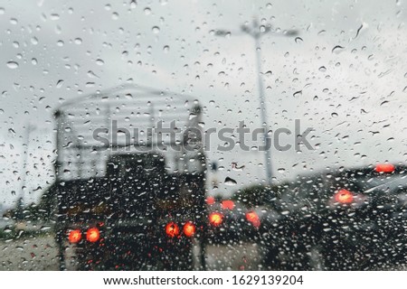 Road view through car window with rain drops driving in rain. Traffic view from car windscreen in rain. Driving in rain. Selective focus.