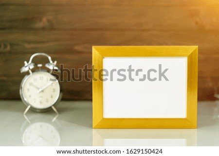 Mockup with blank golden frame and alarm clock on table