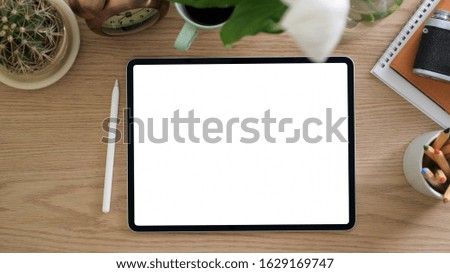 Top view of simple artist workspace with blank screen tablet, stylus, stationery and decorations on wooden table background