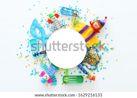 Party colorful noisemaker, mask and cute clown doll over white wooden background . Top view, flat lay