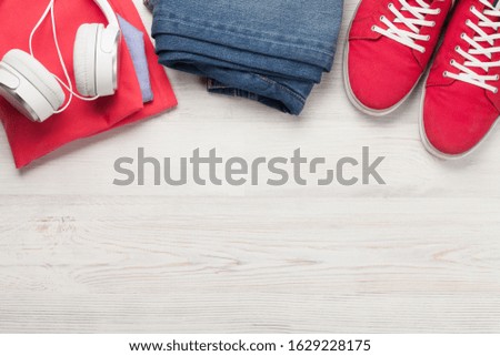 Clothing and accessories. Sneakers, jeans and headphones. Urban outfit for everyday or travel vacation on wooden background with copy space. Top view flat lay