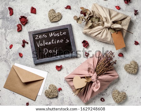 Zero waste Valentine's Day concept. Eco-friendly gift cloth wrapping in Furoshiki style and chalkboard with Zero Waste Valentine's Day letters on gray textured background. Top view or flat lay