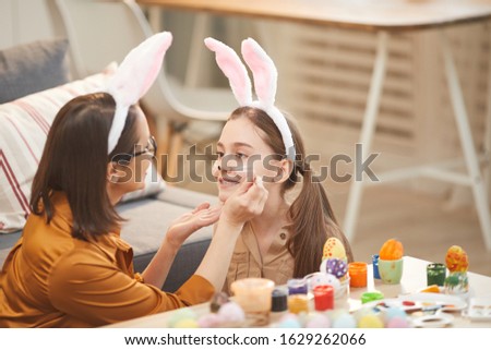 Young mother painting her daughter's face they making rabbit costume for Easter holiday at home