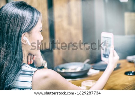 Young beautiful asian business woman relaxing during lunch break, wearing wireless headphones and taking selfies.