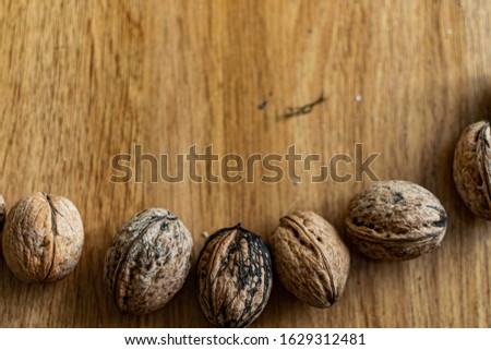Solid and embossed brown-shelled walnuts lie on a wooden table, illuminated by the harsh sunlight
