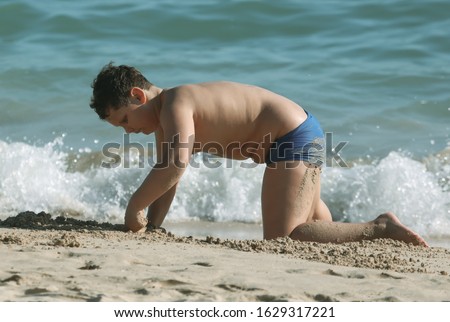 A boy plays in the sand on the seashore.